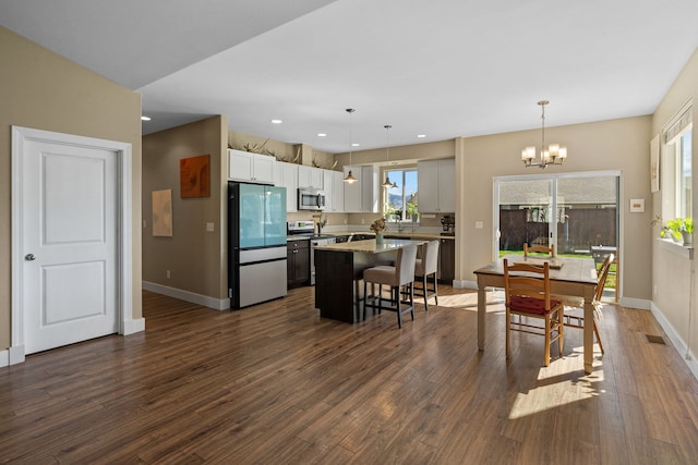 kitchen with dark wood-style flooring, a breakfast bar area, a center island, a chandelier, and stainless steel appliances