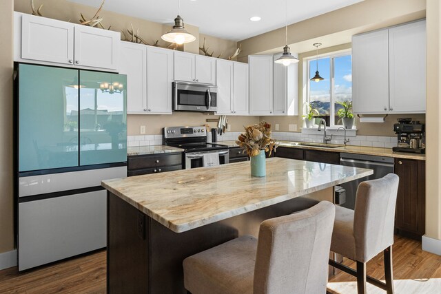 kitchen featuring stainless steel appliances, light stone counters, a sink, and a center island