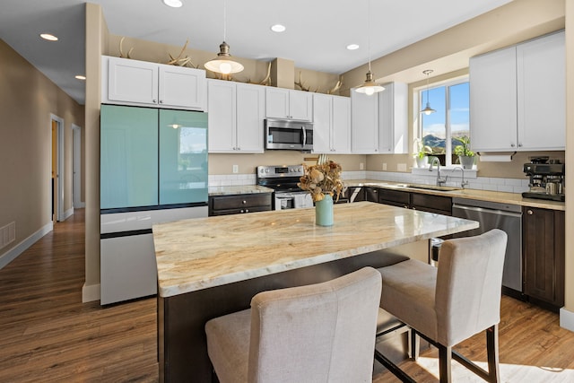 kitchen with appliances with stainless steel finishes, a center island, a sink, recessed lighting, and white cabinetry