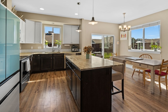 kitchen with fridge, light stone counters, a breakfast bar area, dark wood-type flooring, and stainless steel electric stove