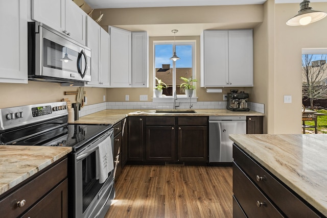 kitchen with appliances with stainless steel finishes, white cabinets, light stone countertops, and dark wood-style floors