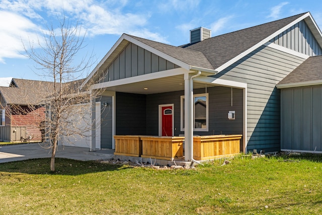 exterior space with board and batten siding, covered porch, a chimney, a yard, and a shingled roof