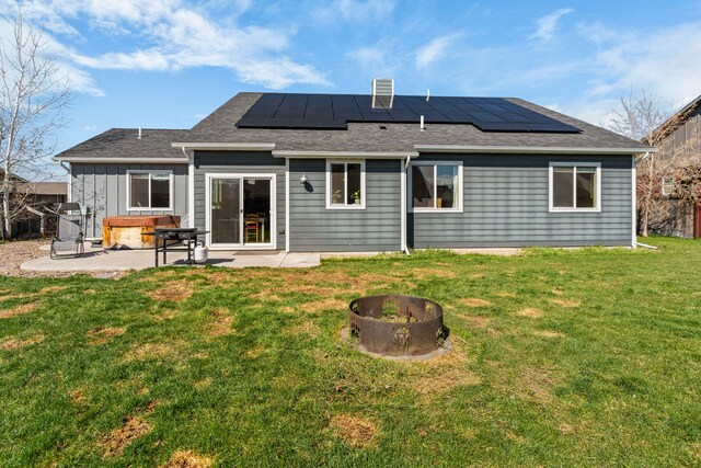 back of house with solar panels, a patio area, an outdoor fire pit, a yard, and a shingled roof