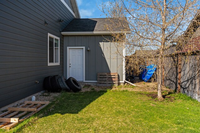 entrance to property featuring a lawn, fence, board and batten siding, and roof with shingles