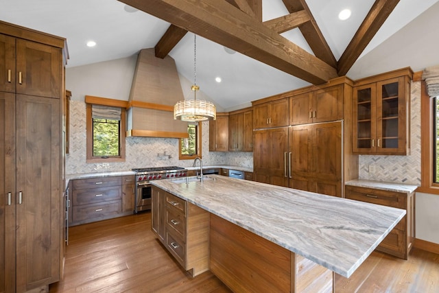 kitchen with lofted ceiling with beams, an island with sink, decorative backsplash, custom range hood, and high end stainless steel range oven