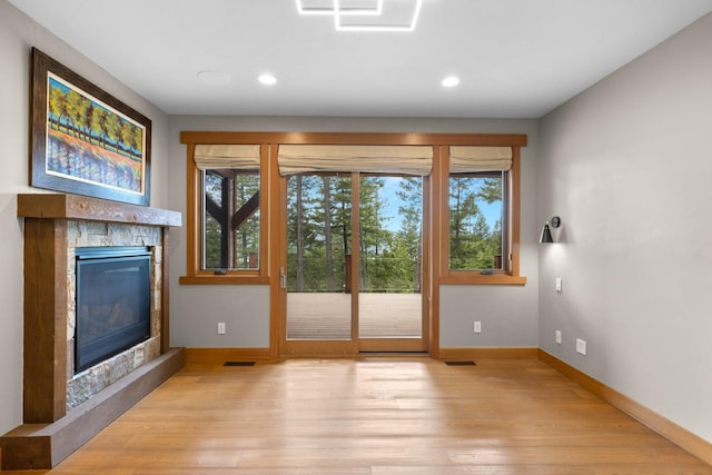 doorway featuring a stone fireplace, light wood-style flooring, baseboards, and a wealth of natural light