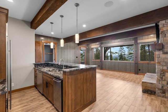 kitchen featuring beamed ceiling, a sink, dark stone countertops, and light wood-type flooring