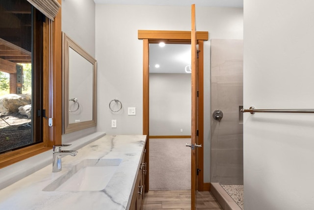 bathroom featuring vanity, baseboards, a tile shower, and wood finished floors