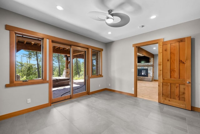unfurnished room featuring a ceiling fan, baseboards, recessed lighting, and a stone fireplace