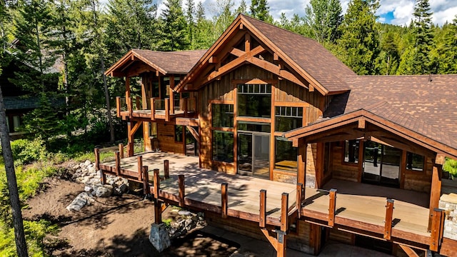 rear view of property featuring board and batten siding, a shingled roof, and a wooden deck