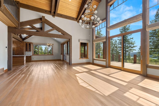 unfurnished living room with high vaulted ceiling, baseboards, wood finished floors, and a notable chandelier