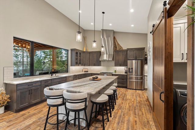 14 Marina Crest Ln, Whitefish, MT 59937 - kitchen featuring washer / clothes dryer, a barn door, wall chimney exhaust hood, stainless steel fridge with ice dispenser, and a sink
