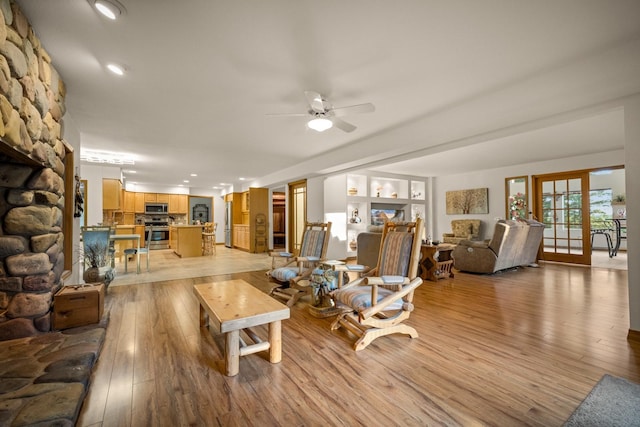 living room featuring recessed lighting, ceiling fan, light wood finished floors, and a stone fireplace