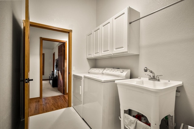 clothes washing area featuring cabinet space, separate washer and dryer, a sink, and wood finished floors