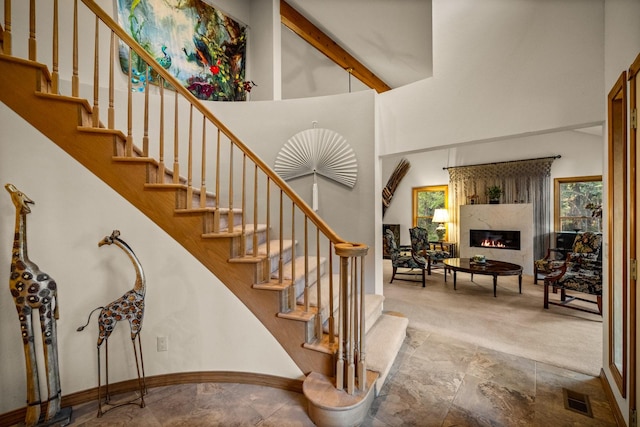 staircase featuring carpet flooring, a large fireplace, baseboards, a towering ceiling, and visible vents