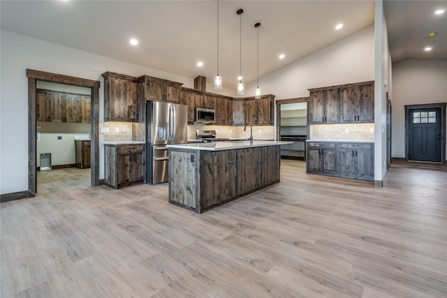 kitchen with a kitchen island with sink, dark brown cabinetry, light countertops, tasteful backsplash, and stainless steel appliances