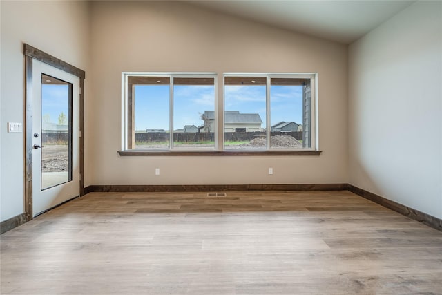 empty room with a healthy amount of sunlight, baseboards, vaulted ceiling, and wood finished floors