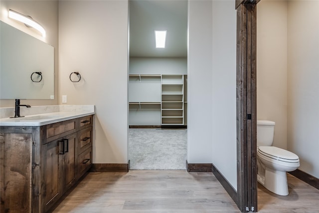 bathroom featuring toilet, baseboards, wood finished floors, and vanity