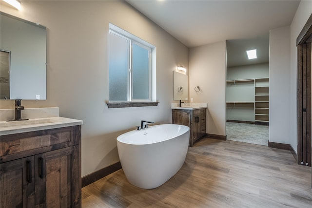 full bathroom featuring a sink, baseboards, wood finished floors, and two vanities