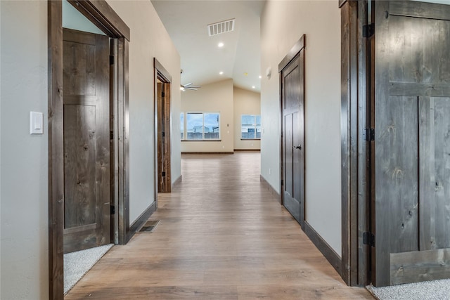 hall with baseboards, lofted ceiling, light wood-style flooring, and visible vents