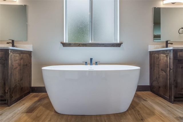full bath featuring a freestanding tub, baseboards, wood finished floors, and two vanities