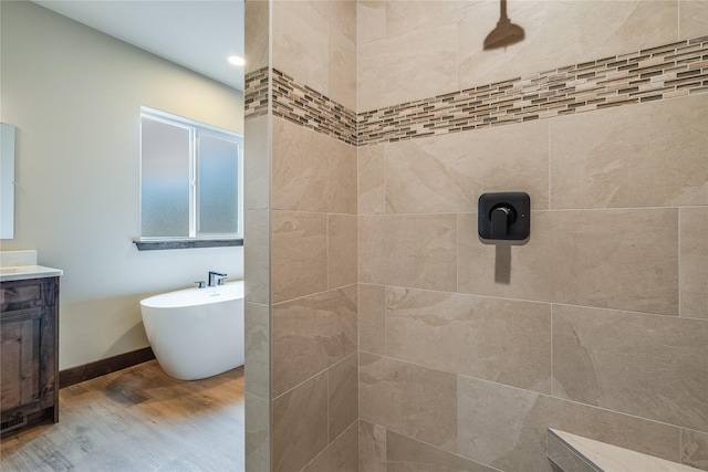 full bath with vanity, wood finished floors, baseboards, tiled shower, and a soaking tub