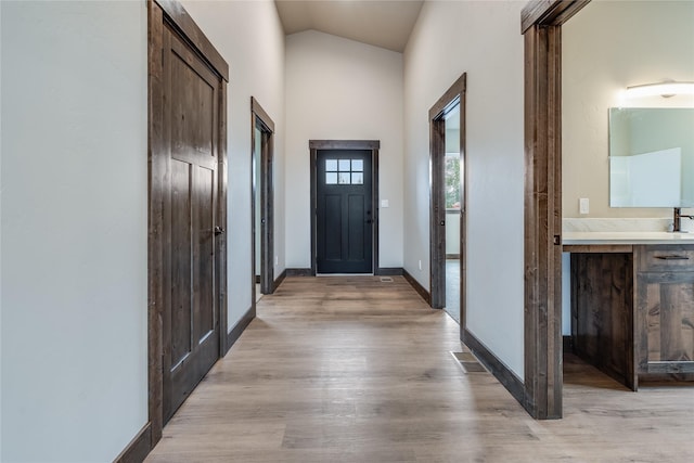 interior space with light wood-type flooring, baseboards, visible vents, and high vaulted ceiling
