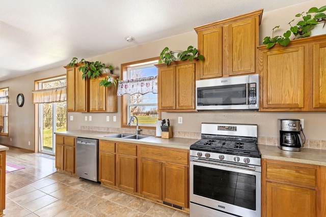 kitchen with brown cabinetry, appliances with stainless steel finishes, a sink, light countertops, and light tile patterned flooring