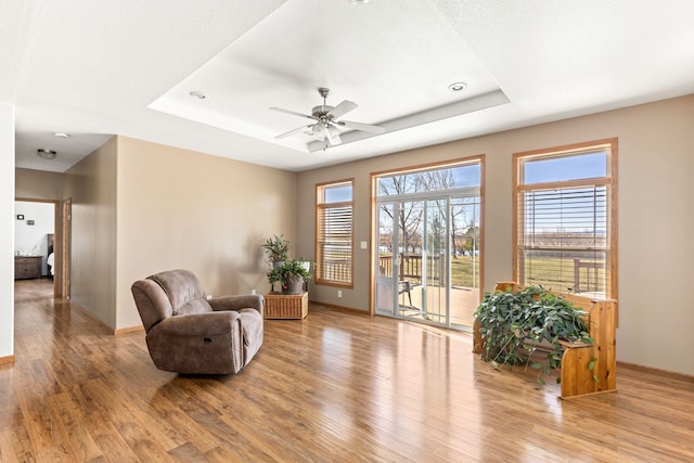 living area featuring baseboards, a tray ceiling, and wood finished floors