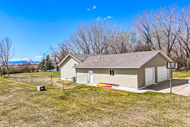 view of property exterior featuring fence, a detached garage, a lawn, and roof with shingles