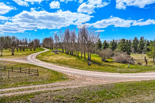 surrounding community with fence, dirt driveway, and a lawn