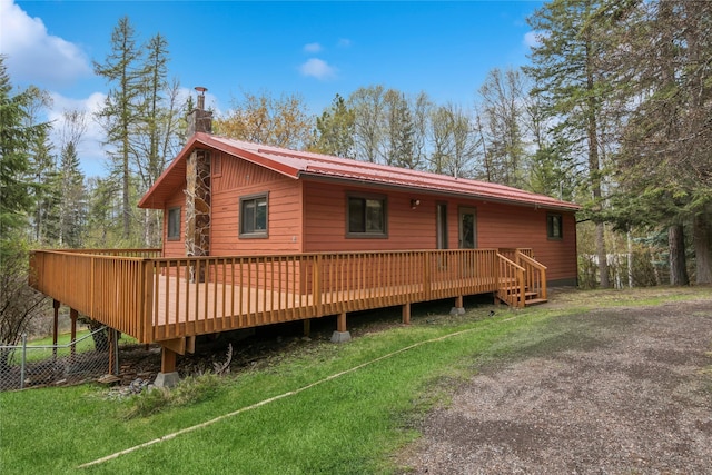 rear view of house with a lawn, fence, a deck, and metal roof