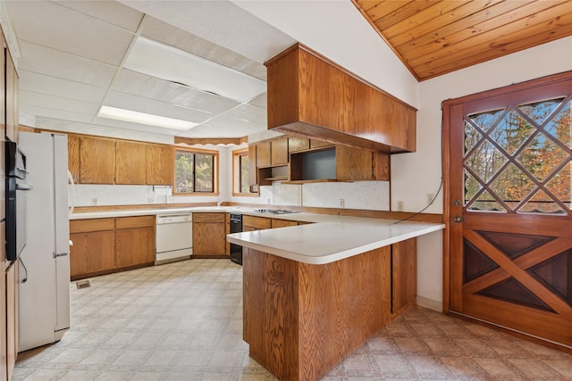 kitchen with brown cabinetry, a peninsula, white dishwasher, light floors, and stainless steel gas stovetop