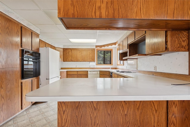 kitchen featuring light countertops, a peninsula, light floors, a drop ceiling, and white appliances