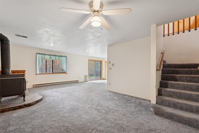 unfurnished living room featuring visible vents, baseboard heating, a wood stove, stairway, and carpet