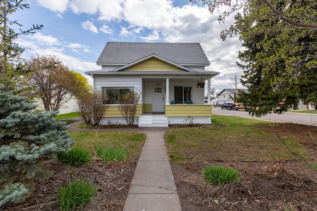 bungalow-style house featuring a front lawn, roof with shingles, and covered porch