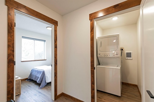 laundry room featuring baseboards, stacked washer / dryer, laundry area, and wood finished floors