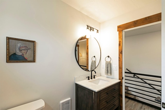 half bath featuring vanity, wood finished floors, visible vents, and toilet