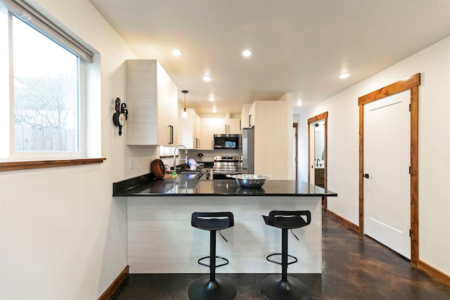 kitchen featuring appliances with stainless steel finishes, dark countertops, a sink, baseboards, and a peninsula