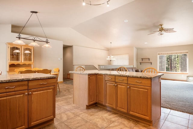 kitchen with pendant lighting, light stone countertops, ceiling fan with notable chandelier, open floor plan, and lofted ceiling