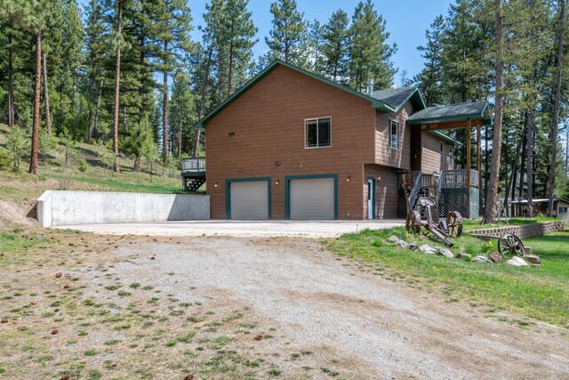 view of side of property featuring a deck, an attached garage, and dirt driveway