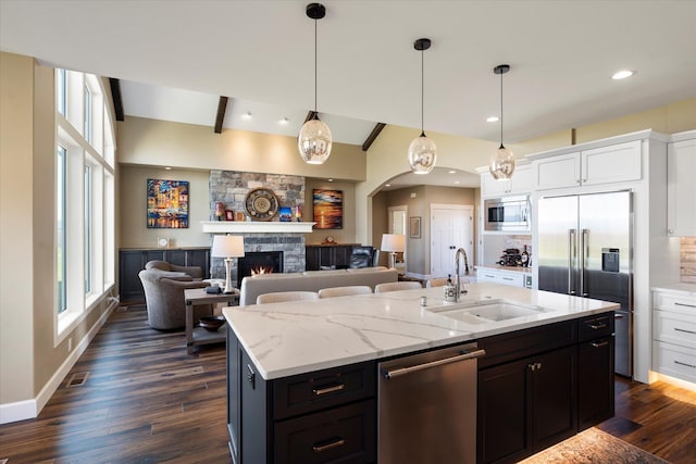 kitchen with dark wood-style flooring, built in appliances, a stone fireplace, arched walkways, and a sink