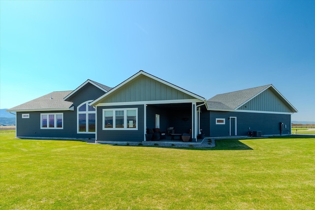 rear view of house featuring board and batten siding, roof with shingles, and a yard