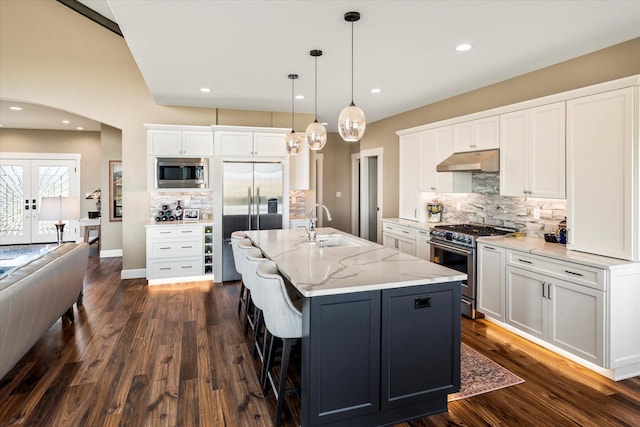kitchen featuring decorative backsplash, arched walkways, a sink, built in appliances, and under cabinet range hood