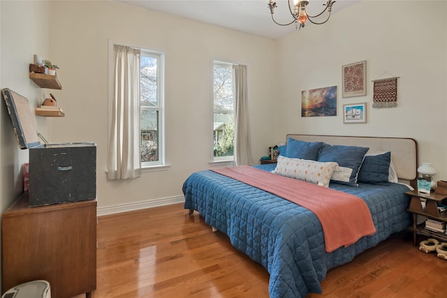 bedroom with baseboards, an inviting chandelier, and wood finished floors