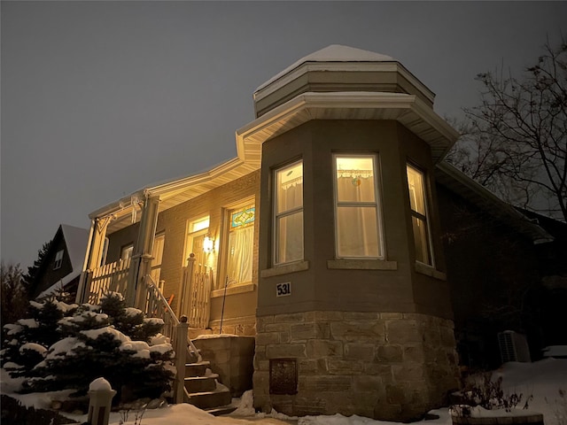 property exterior at night featuring a porch, stairs, and stone siding