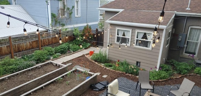 view of property exterior featuring a fenced backyard, a shingled roof, a garden, and a patio area