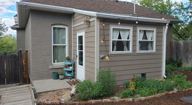 view of property exterior with brick siding, fence, and a shingled roof