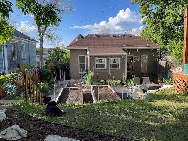 back of property featuring a shingled roof, a garden, and a fenced backyard