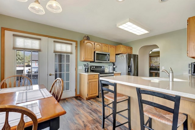 kitchen with dark wood-style flooring, a kitchen bar, light countertops, arched walkways, and appliances with stainless steel finishes